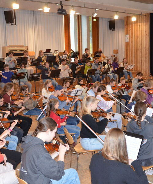 Zu sehen sind die Jugendlichen mit Instrumenten in einer Orchesterformation bei einer Probe in einem Musiksaal