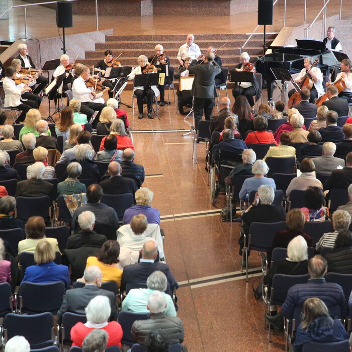 Zu sehen sind Zuschauer die einem Orchester zuhören.