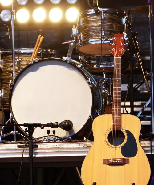 Auf dem Bild zu sehen ist ein Set einer Band, bestehend aus Gitarre, Schlagzeug und Mikrofonen auf einer Bühne