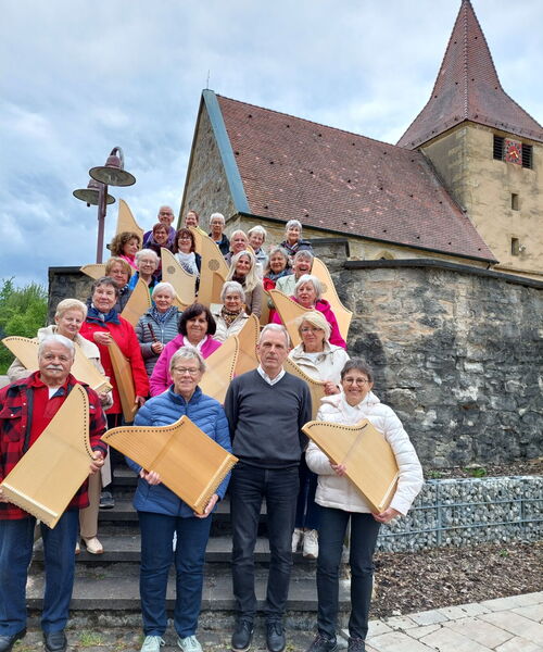 Zu sehen sind Personen mit Veeh-Harfen auf einer Treppe vor einer Kirche stehen